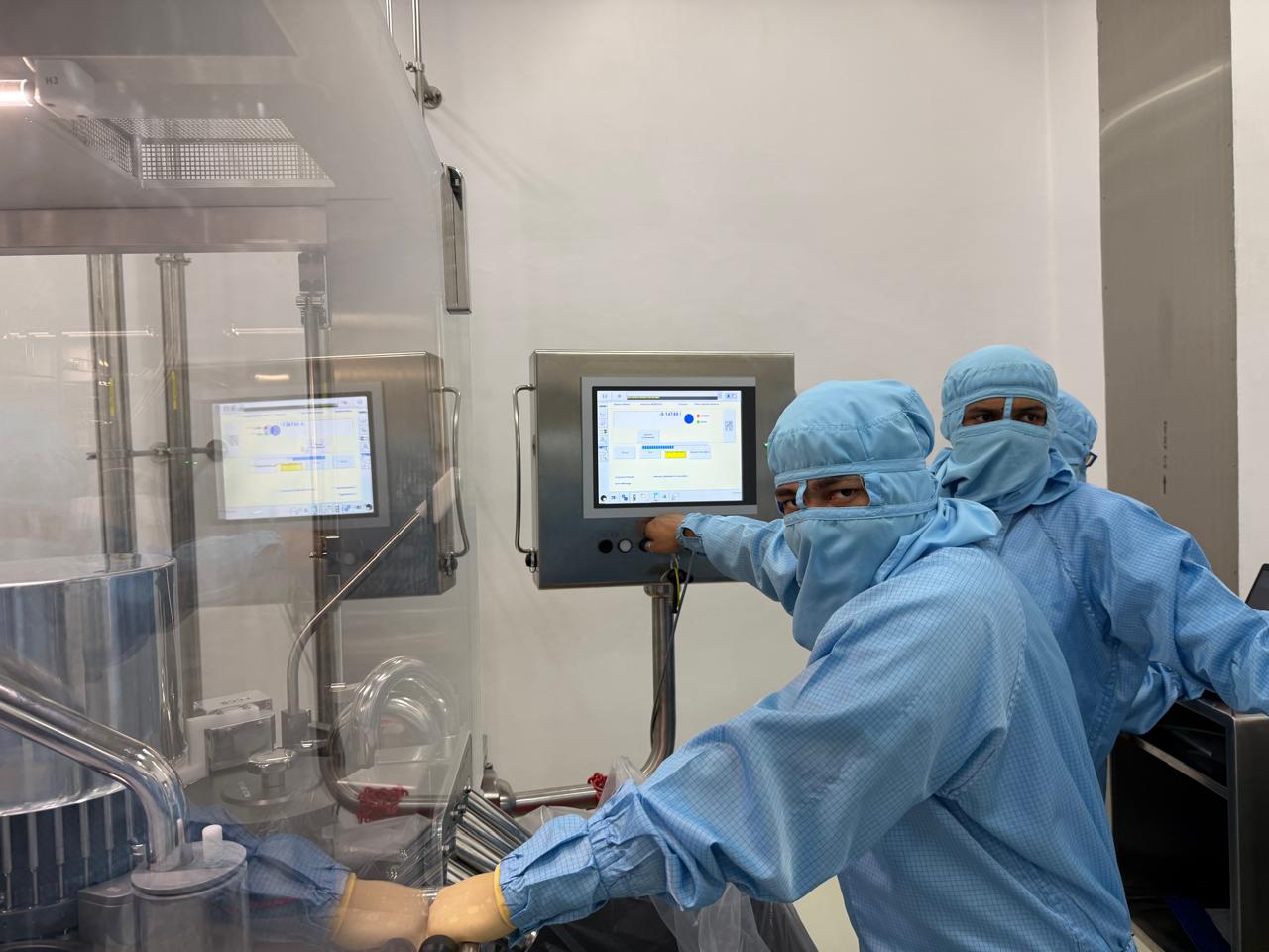 Engineers operating inspection controls beside pharmaceutical machinery